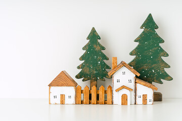 Naklejka premium Happy New Year and Merry Christmas postcard. Festive white background with toy wooden house, snow, rustic christmas tree, village and decoration. Copy space for winter holidays greeting card. 