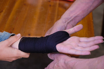 Obraz premium The black elastic bandage on the woman's hand. An experienced old man applying a medical bandage on the hand of a young woman at home.