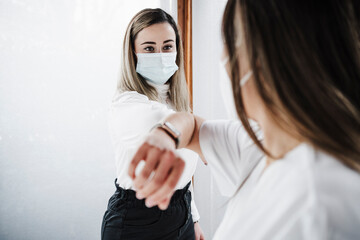 Female patient wearing protective face mask doing elbow bump with doctor at hospital