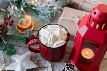 Winter hot drink, cacao with marshmallows and cinnamon or spicy hot chocolate in red cup and Christmas garland. Festive vintage background.