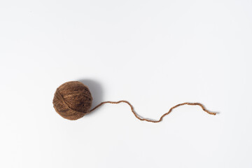 Dark brownish ball of yarn with loose thread on white background