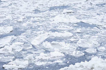 Snow-covered ice on the river during a snowfall. Winter texture. Suga and ice floes.