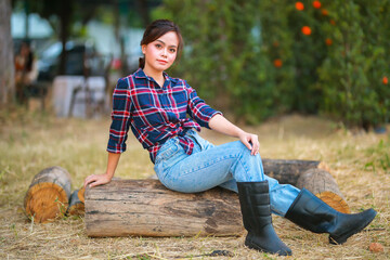Portrait of cowgirl. Beautiful Young asian woman gardener in red plaid shirt at summer sunset.