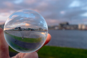 View through glass ball on river Corrib and Galway city, the Long walk along the river. Dramatic sky. Creative photography.