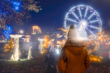 Teenager girl in focus, back to viewer, Christmas decorated park out of focus in the background...