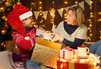 Portrait of mother and son in new year decoration. Woman and teen boy opening the box, take out gifts, having fun and laughing. Holiday lights, gifts and christmas tree decorated with toys.