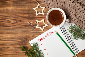 Santa's Wish List at notepad and coffee cup, scarf, fir branches on wooden background