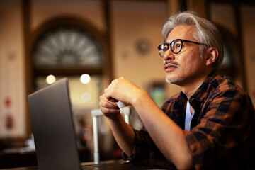 Businessman working on laptop in cafe. Handsome senior man enjoying in fresh coffee..