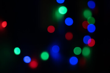 Fototapeta premium Defocused bokeh lights on black background, an abstract naturally blurred backdrop for Christmas eve or birthday party. Festive light texture. Colorful garland in blur. Overlay effect for design