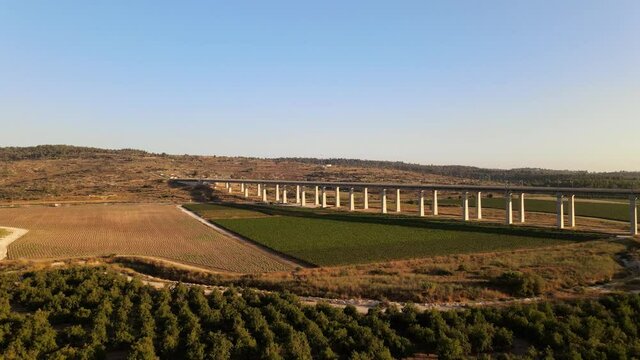 Aerial view of a long road bridge over a landscape with fields and meadows at sunset in Israel