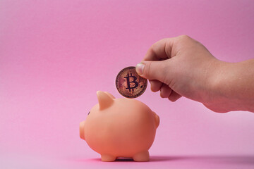 A man's hand puts a bitcoin into a piggy bank.