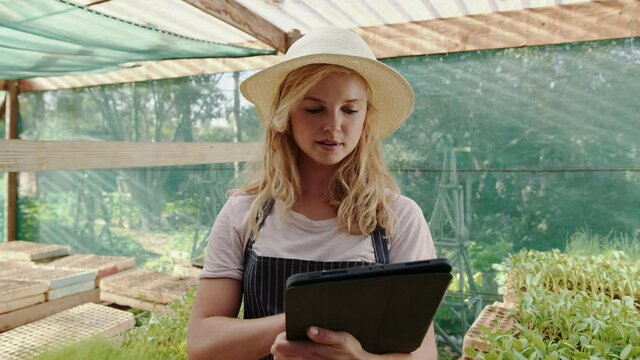 Caucasian female farmer working in green house typing on digital tablet