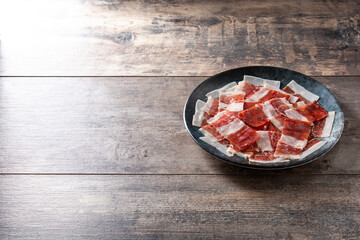 Spanish serrano ham slices on black plate on wooden table. Copy space