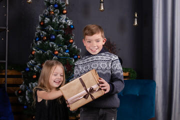 Fototapeta na wymiar happy kids playing with christmas presents. brother and sister near christmas tree giving new year gifts to each other. family time. siblings love