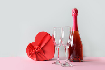 Valentine's day compositon of champagne or sparkling wine, heart gift box, wine glasses on blue background. Greeting card with copy space.