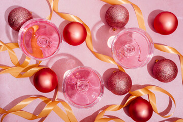 Pink champagne in luxury crystal glasses and christmas baubles with golden ribbon decor. Top view....