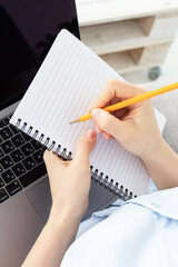 Concept for online courses, web event, online learning, goal writing, freelancing, distance work, online platform. Female hands are holding a notepad and a pencil over the computer keyboard. Indoors.