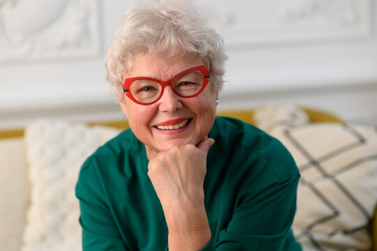 Smiling 60s middle aged woman looking at camera. Happy mature elegant old lady posing at home. Headshot close up portrait