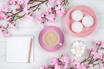 Coffee cup with marshmallow in the morning for breakfast. Blank notebook with pen. Diary, planning concept. Romantic spring mockup with copy space. Cherry blossom on white wooden background. Flat lay.