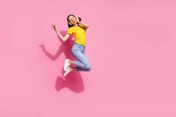 Fototapeta na wymiar Photo of sweet dreamy young woman wear yellow outfit jumping high listening songs headphones empty space isolated pink color background
