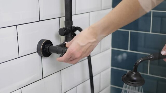 woman adjusts the water temperature with tap in the shower