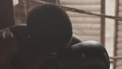 Slowmo medium close up of tired African-American male boxer trying to take breath sitting in corner at boxing ring after hard training or sparring