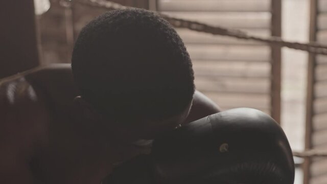 Slowmo medium close up of tired African-American male boxer trying to take breath sitting in corner at boxing ring after hard training or sparring