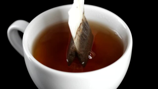 Making tea with tea bag in white cap, close up. Putting tea Bag Into  Cup Full of Hot Water. 4K UHD video