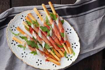 Antipasto platter cold meat plate with grissini bread sticks, prosciutto, slices ham, and arugula on wooden background. Meat appetizer. Top view