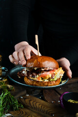 Cooking. Burger with bacon and shrimp in the hands of a chef. On a dark background.