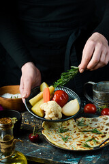 Pickled cucumbers, tomatoes, onions and cabbage on a plate in the hands of a chef on a black background.