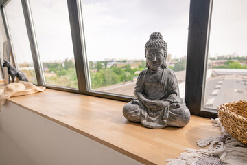 Buddha Figurine in Meditation Pose on a Wooden Windowsill Next to a Large Window. Close-up . 