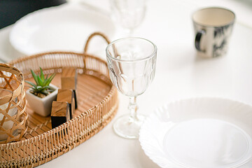 Served and Decorated White Table with Glasses, Plates and a Mug. Table Decoration with Wicker and Wooden Decor Elements