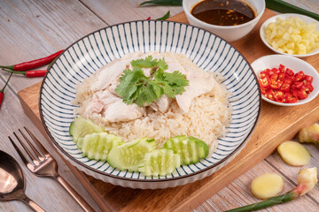 Steamed rice topped with chicken on wooden background, Hainanese chicken rice served with chili sauce on a wooden background.