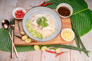 Steamed rice topped with chicken on banana leaves, Hainanese chicken rice served with chili sauce on a wooden background.