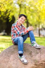 Smiling boy wearing casual clothes while sitting on a rock at city park