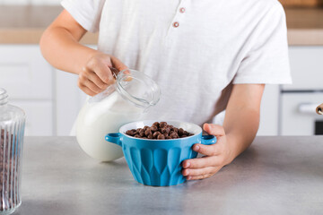 Obraz na płótnie Canvas A child pours milk from a jug into a bowl of chocolate flakes. Child's breakfast.