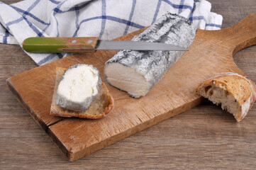 Bûche de fromage de chèvre cendrée sur une planche à découper avec un couteau et du pain