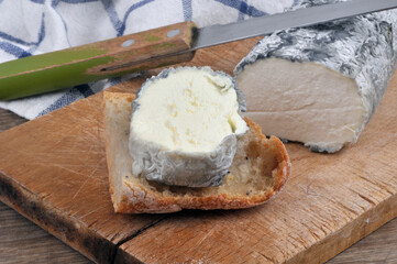 Bûche de fromage de chèvre cendrée sur une planche à découper avec un couteau et du pain