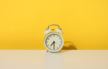 a round alarm clock stands on a white table, half past seven in the morning. Yellow background