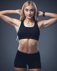 Studio portrait of a young pretty girl with a sporty physique on a studio background. Beautiful blonde in a top and sports shorts. Sportswear for athletics.