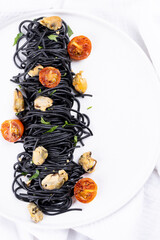 Squid ink pasta with seafood: mussels on a white plate on a white wooden background
