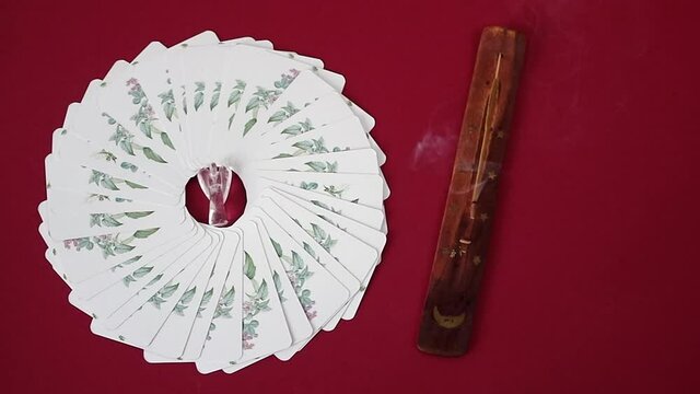 Incense stick burning, white cards deck in a circle with clear quartz angel in the centre, on burgundy red background