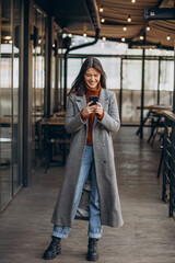 Young woman wearing grey coat and walking in the street and using phone