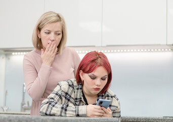 Shocked mother looks at the  screen of smartphone that her teen daughter uses