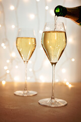 Pouring champagne or sparkling wine into a flute glass, bokeh lights in the background, Christmas or New Year holiday atmosphere