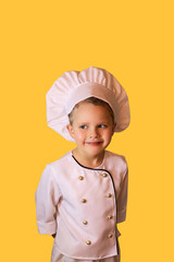 Smiling child in white chef uniform with a funny hat. Cheerful yellow background.