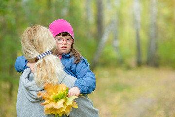Mother holds in her arms daughter with Downs syndrom  at autumn park. Empty space for text