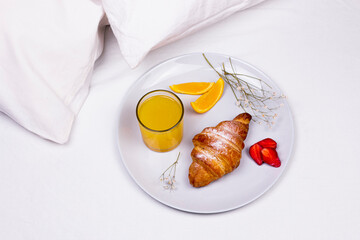 Romantic morning breakfast in bed. Orange juice, croissant and strawberry on the plate.