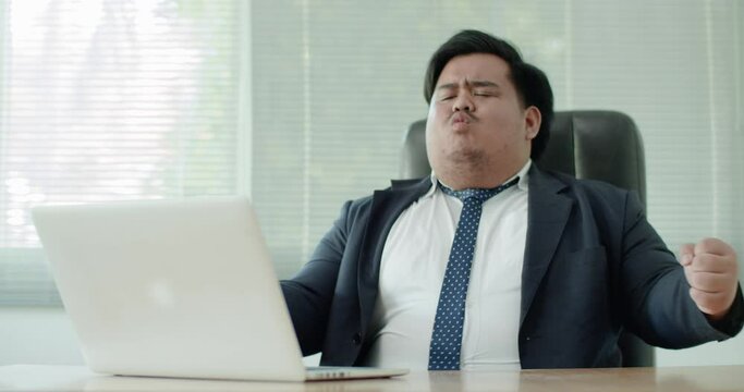 Asian business man which has a fat figure and funny personality, wearing a suit like an executive or a manager using a laptop in the office. Later, his business success made him excited.